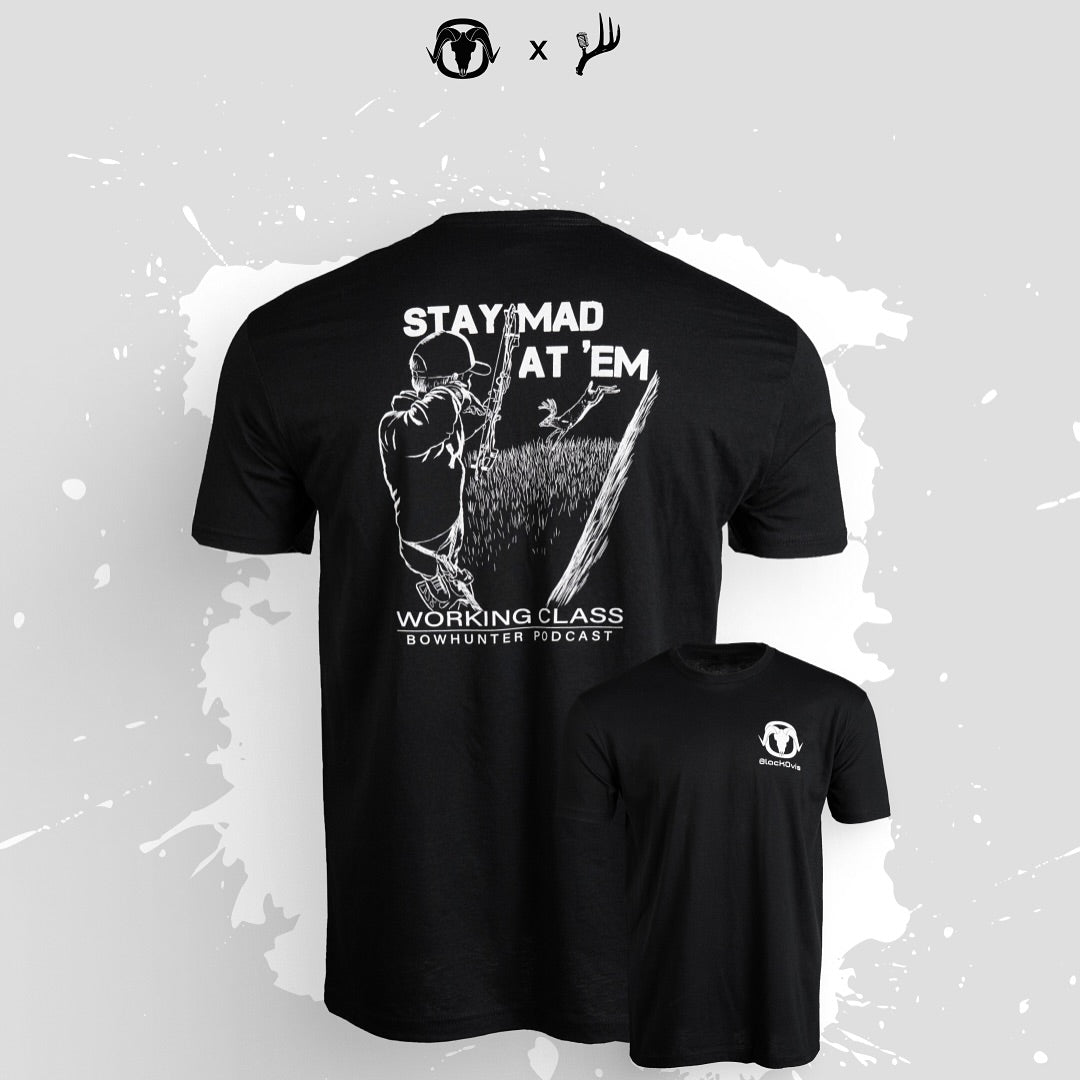 Black short-sleeve t-shirt shown from the back and front on a light gray background with white paint splatter. The back has a large white graphic of a bowhunter aiming a bow, with the text 'STAY MAD AT 'EM' and 'WORKING CLASS BOWHUNTER FIDOCAST'.