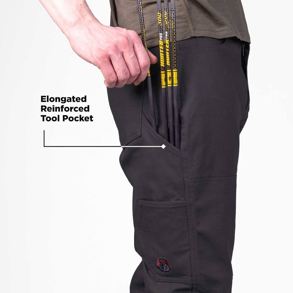 Close-up of a person wearing dark charcoal work pants, showing an extended side pocket holding several black and yellow poles. Text on the image highlights the elongated reinforced tool pocket.