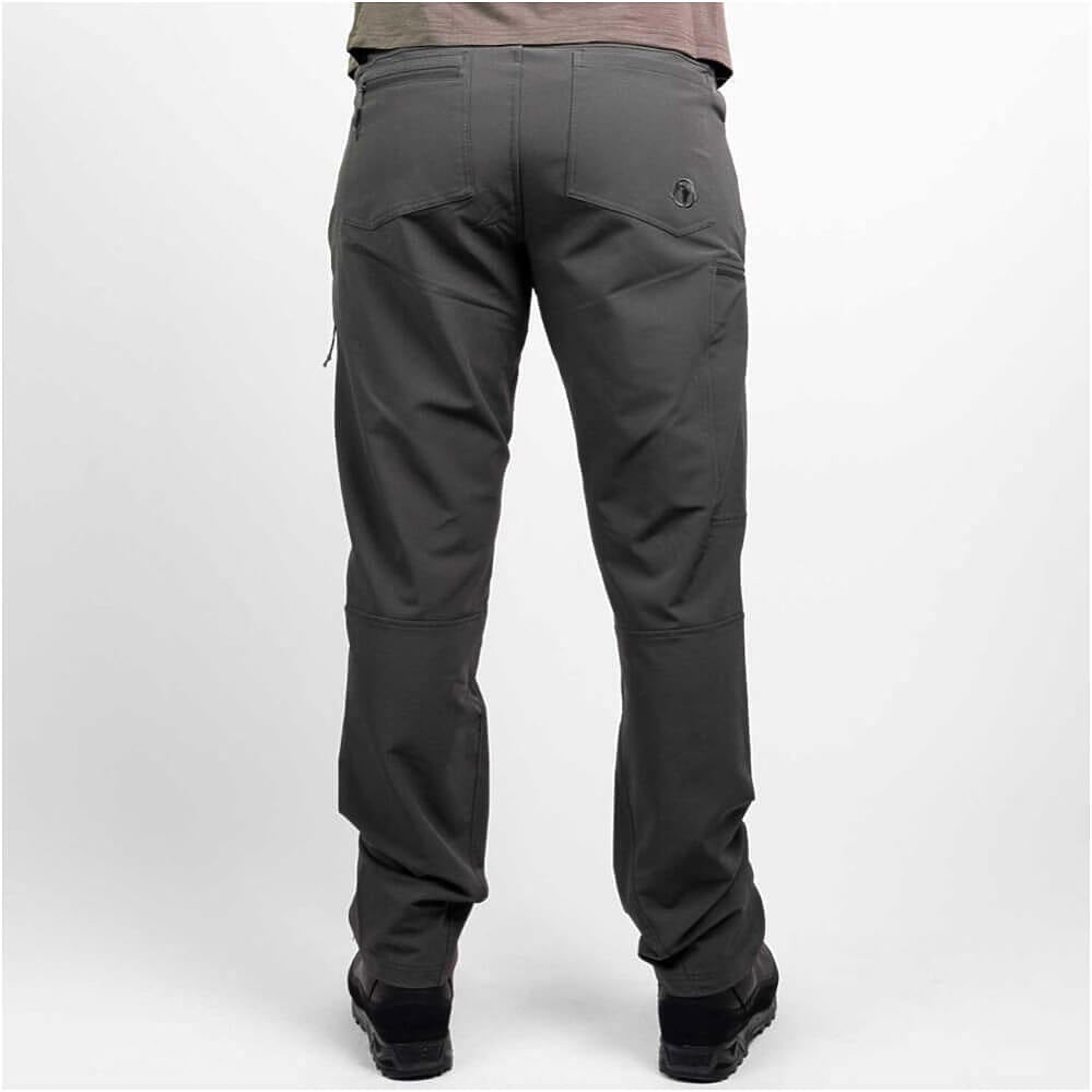 Rear view of a person wearing dark gray technical pants with black boots against a light gray studio background.
