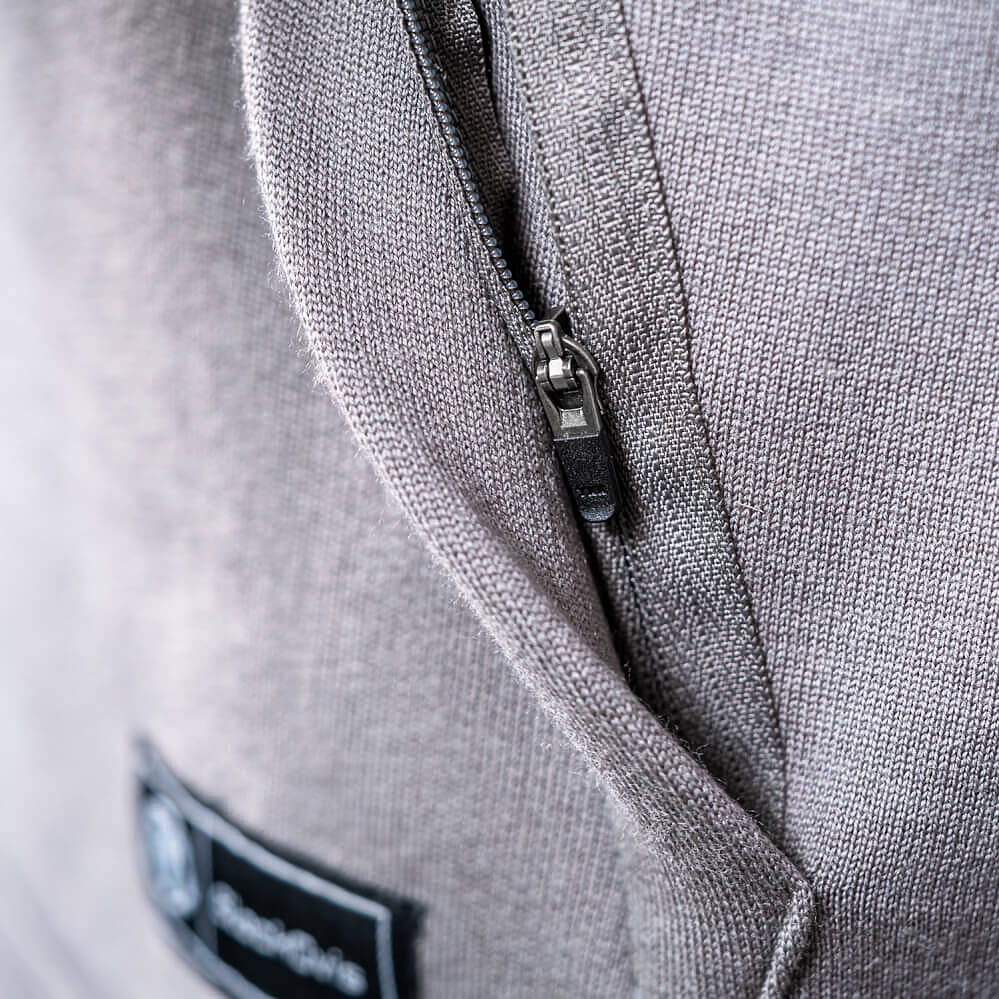 Close-up of a gray knit garment showing a black zipper with a silver metal pull and a small black brand patch near the bottom left.