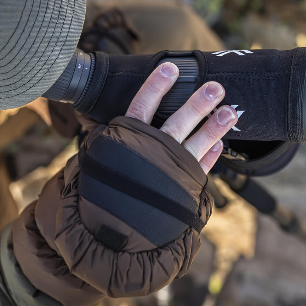 A close-up of a person wearing a brown insulated glove while holding a black camera lens protector with a white logo.