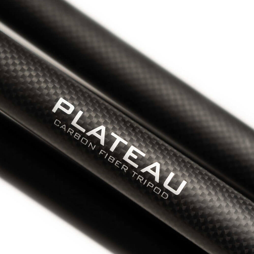 Close-up of two black carbon fiber tripod legs with white text reading 'PLATEAU' and 'CARBON FIBER TRIPOD' on a clean white background.