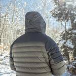 A person viewed from behind wearing a dark gray hooded puffer jacket in a snowy outdoor setting with trees in the background.