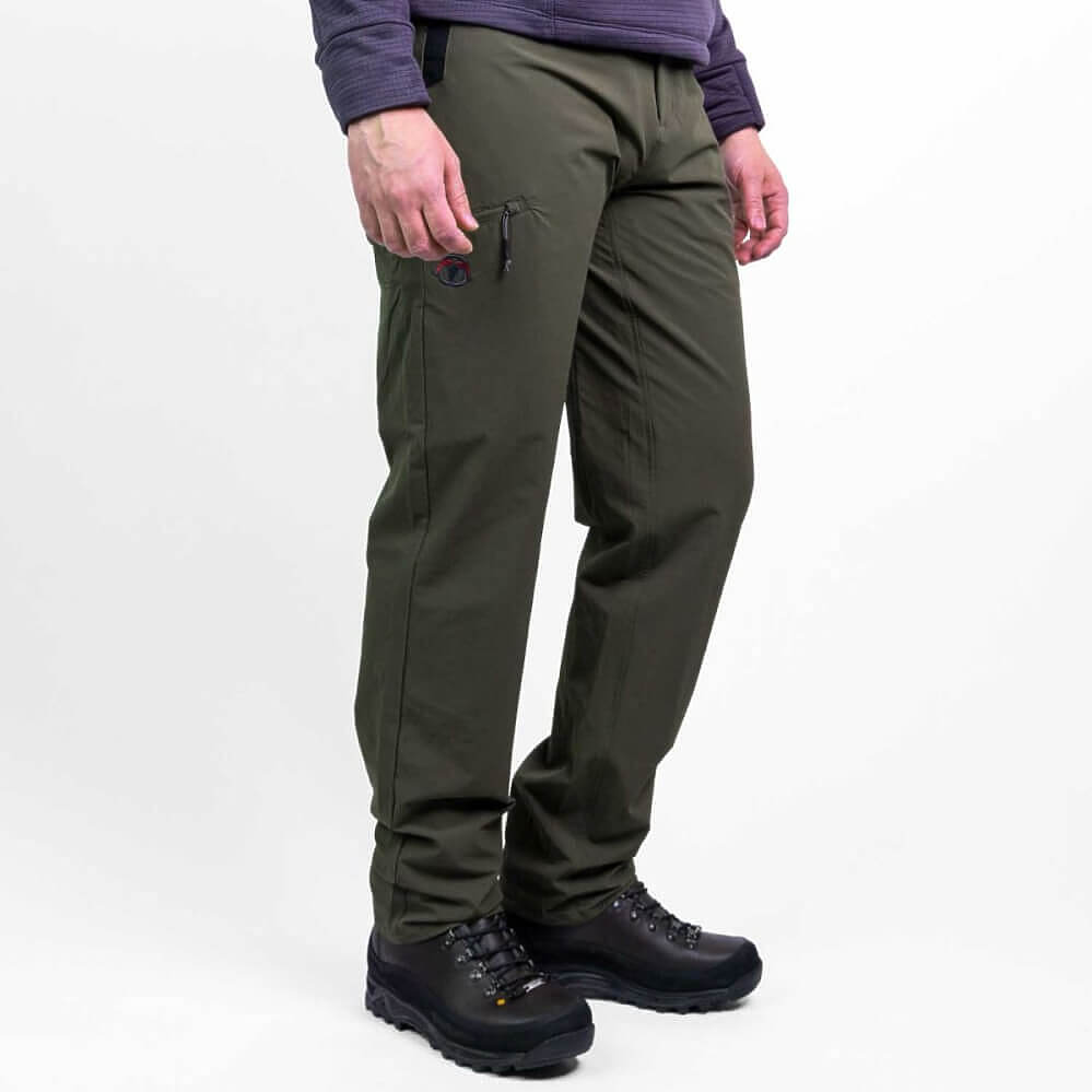 A person wearing olive green technical pants with black hiking boots and a dark purple long-sleeve top, shown from the waist down against a plain white studio background.