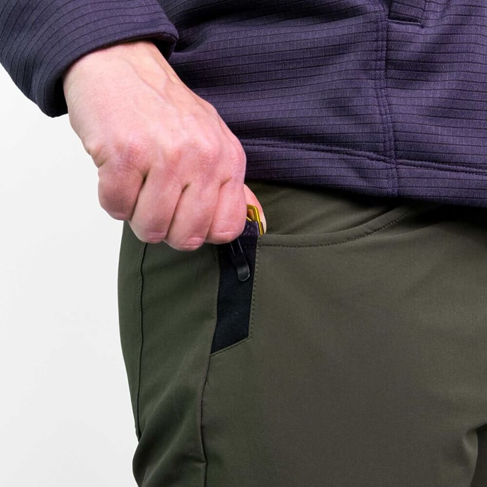 Close-up of a person's hand pulling a black zipper on an olive green pants leg, wearing a dark purple ribbed fleece jacket.