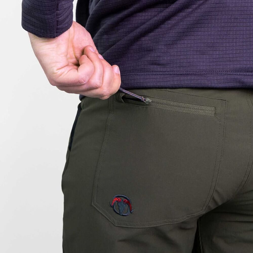 Close-up of a person wearing dark olive green technical pants with a zippered pocket and a small circular logo patch, paired with a dark purple ribbed top.