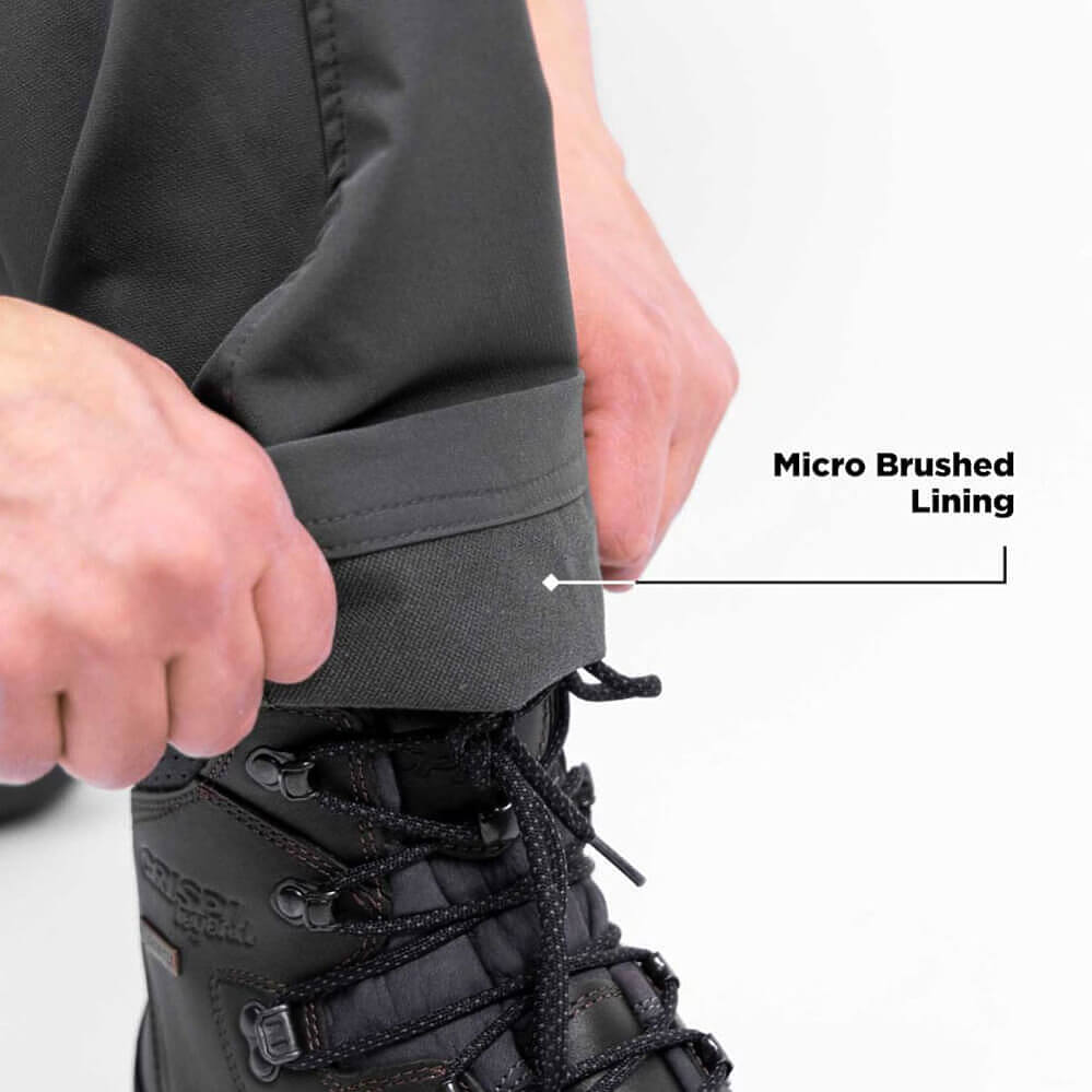 Close-up of a person's hands pulling up the cuff of dark gray pants to show the micro brushed lining, with a black lace-up boot visible underneath. Text on the image reads 'Micro Brushed Lining'.