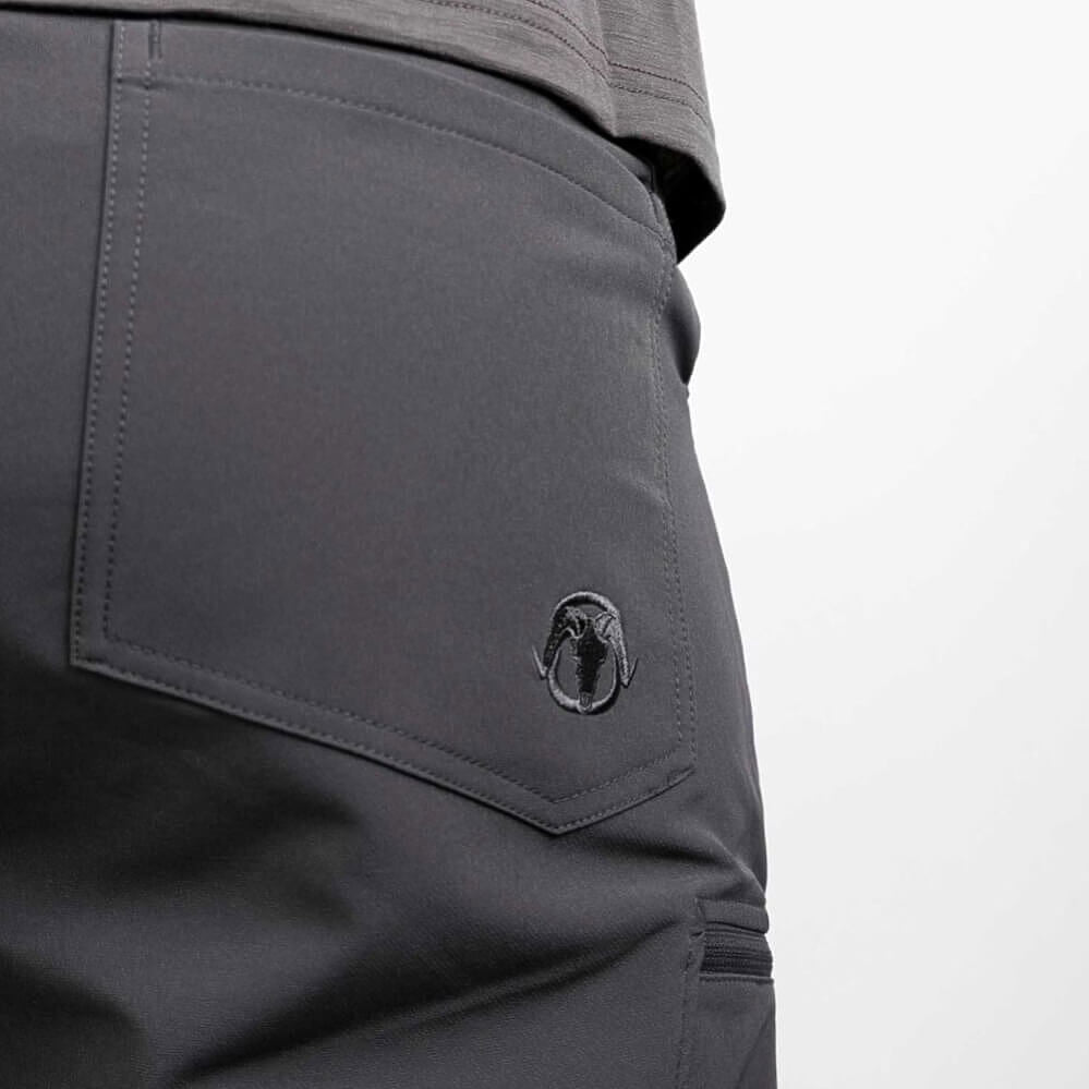 Close-up of dark gray outdoor pants showing a side pocket with a black embroidered circular logo and a gray shirt hem at the waist.